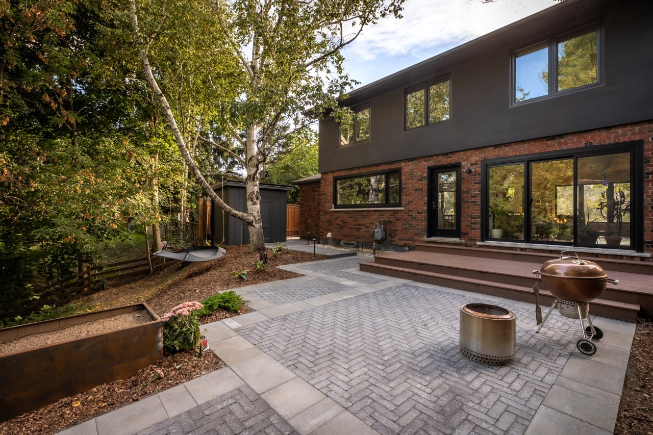 Professionally designed backyard patio with herringbone pavers, composite steps, integrated planting beds, and defined outdoor living space